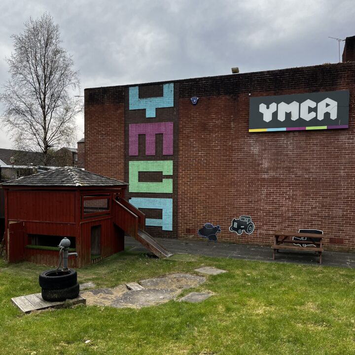 The side of a YMCA youth club, a plain brick building with an angular version of the YMCA logo made out of painted brick vertically spanning the height of it