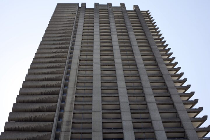 A ground-level shot of one of the concrete towers at the Barbican Estate. Many floors repeat up towards the top of the image, with the shapes of balconies visible.