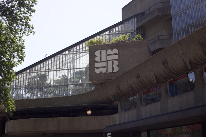 Shot focused on the 4 B's of the Barbican logo, with some prominent concrete in the foreground and the glass of the conservatory in the background.