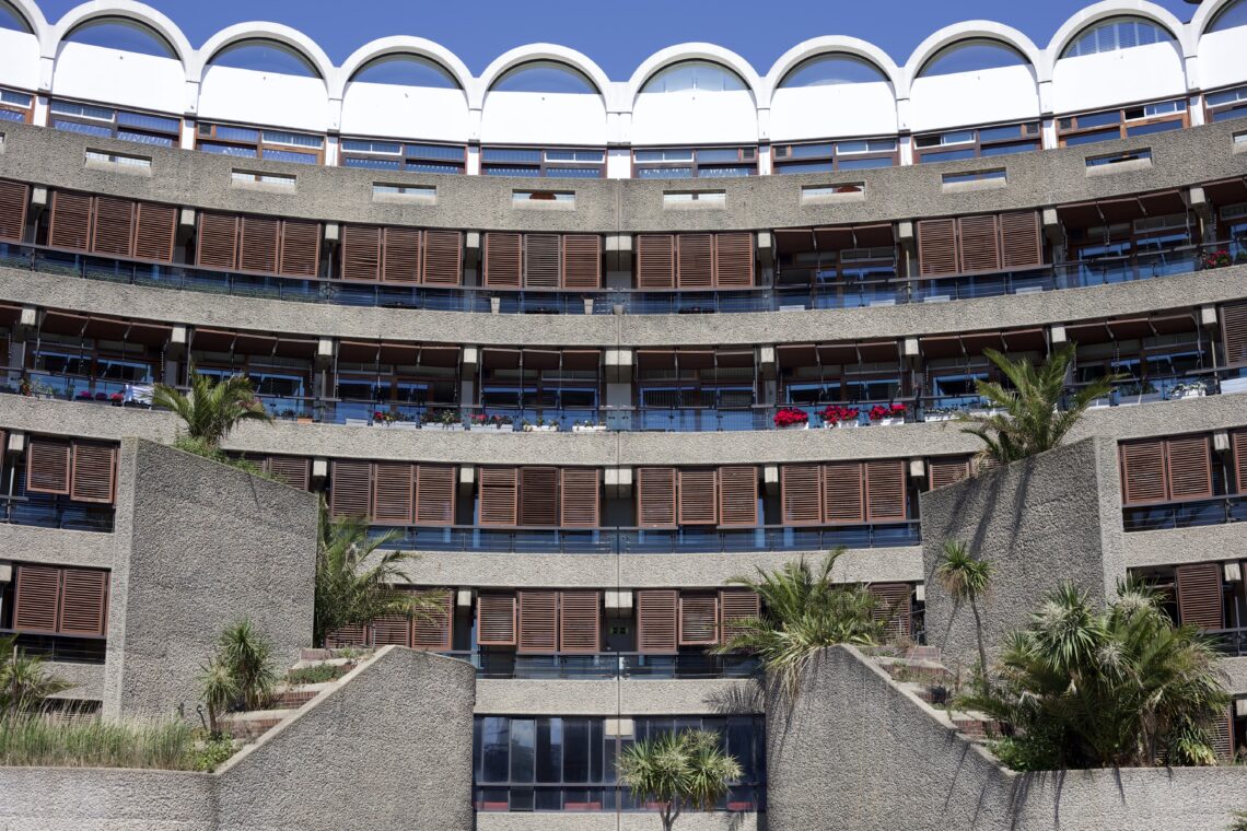 A shot of balconies, mostly covered with wooden shutters, at the circle-shaped building at the Barbican estate. In the foreground, concrete planters.