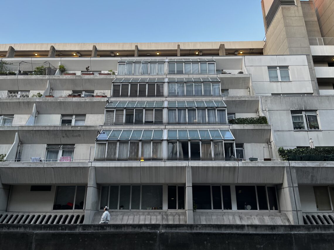 A detail photo of the Brunswick Centre. It is a concrete structure painted white, ziggurat-style, about 6 stories. The photo shows a front-on view of 4 glass conservatories coming out the face of the building on each floor.