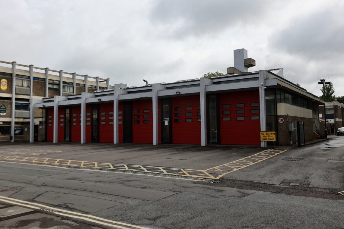 This photo focuses on the fire station garage, with 6 red shutters for fire truck, framed by an external concrete frame painted white.