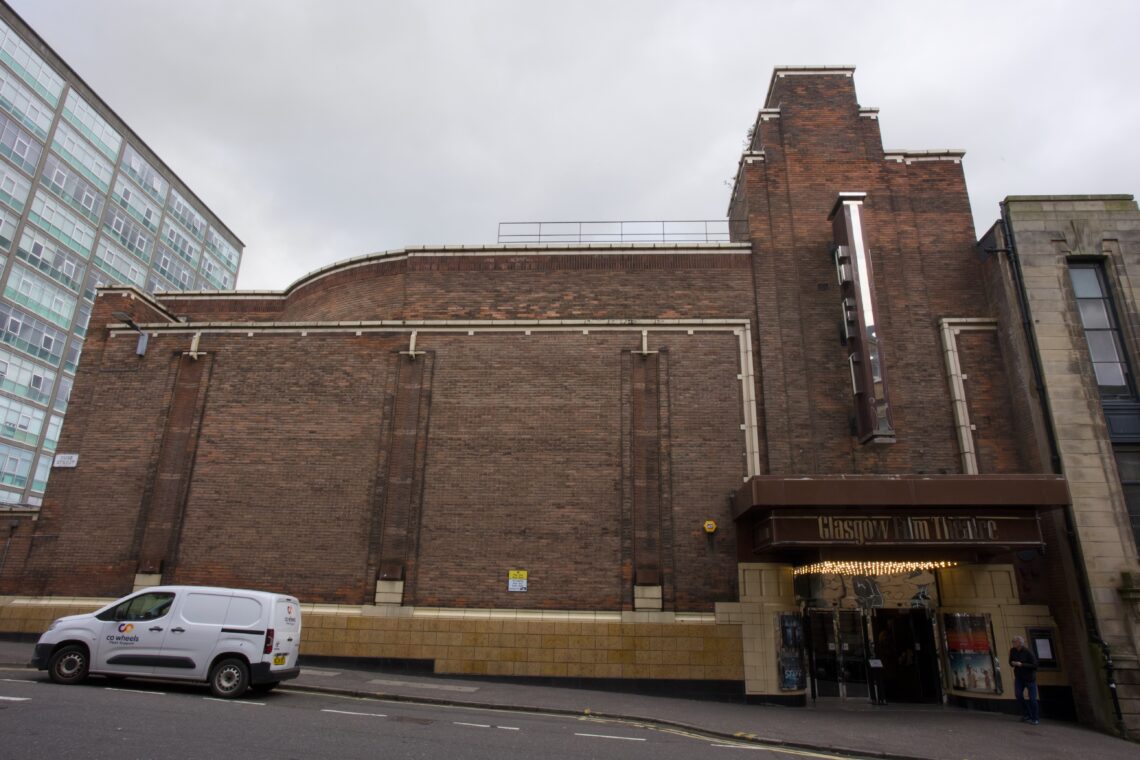 A large red-brick Art Deco building with Christown on a vertical sign above the entrance canopy. Glass doors lead inside. A white van is parked on the street in front, and a grey modern building is visible to the left. Sky is overcast.